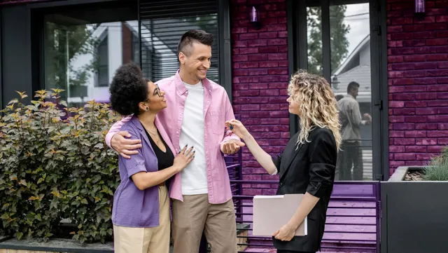 A real estate agent hands keys to a couple standing outside their new home.