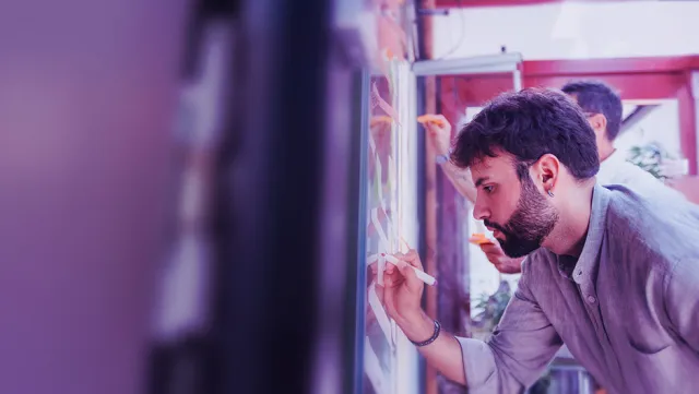 Team member writing ideas on a glass board during a brainstorming session