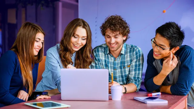 Image of four friends smiling while looking at a laptop
