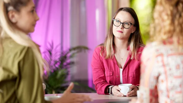 Image of woman holding a coffee cup while listening to officemates