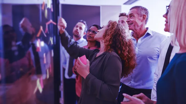 Group of diverse businesspeople strategizing with sticky notes on a glass wall while working together in a modern office
