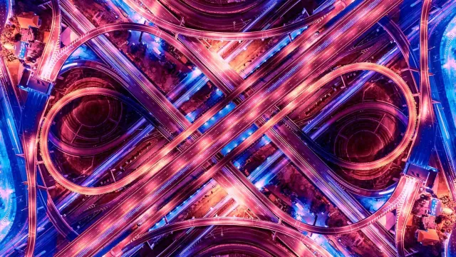 Aerial view of a multi-level highway interchange lit with vibrant purple and blue lights at night.