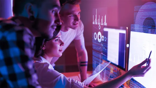 Data analytics team analyzing digital dashboards on large computer screens in a modern office