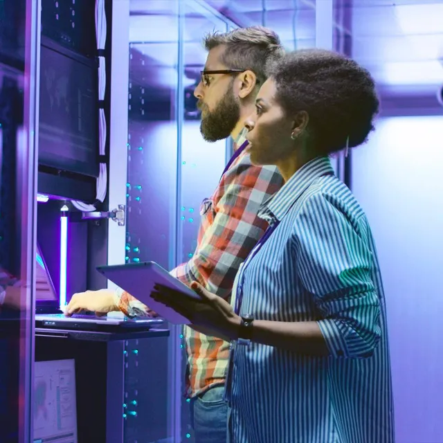 Image of two office workers typing on a laptop in a mainframe room