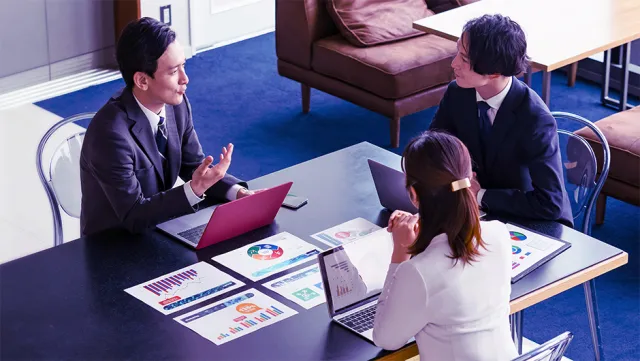 Business professionals meeting around a table reviewing analytics charts and laptops