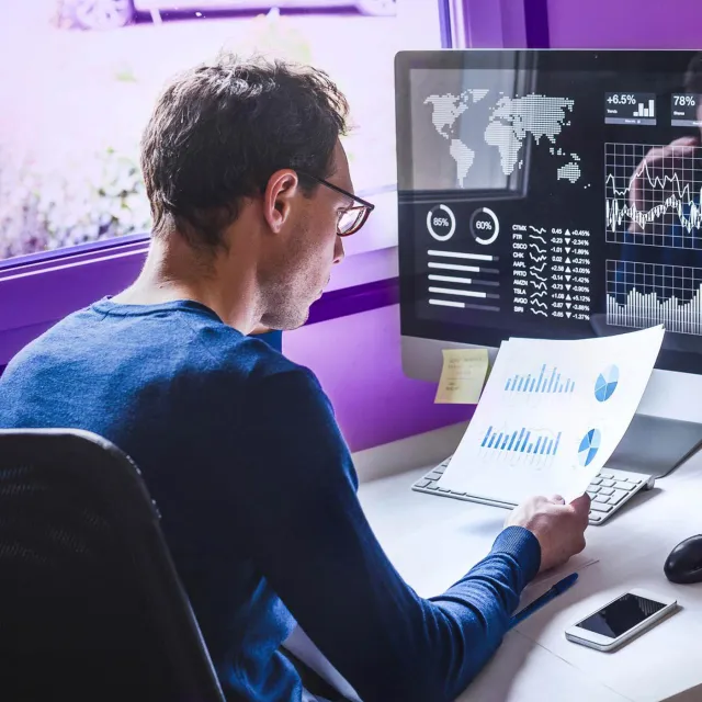 Bank analyst looking at data on both digital screen and printed report