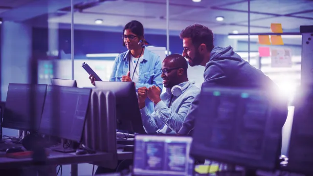Image of three officemates discussing and happy looking at a monitor