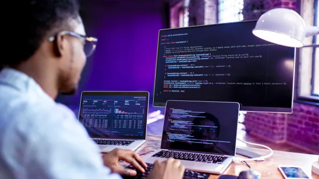 Image of man working in front of three devices