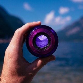 Someone holding a camera lens over a lake