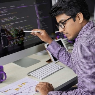 Image of man comparing document report and code in monitor