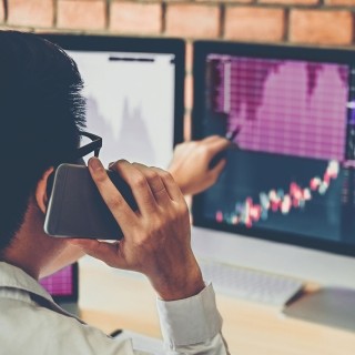 Image of man on phone pointing at monitor displaying various graphs