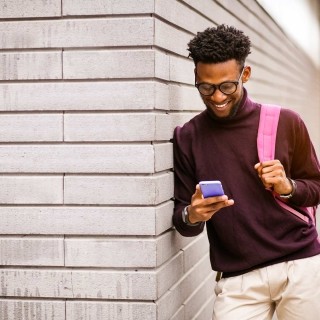 Image of man texting leaning on wall