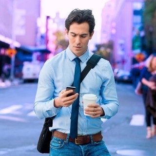 Image of man looking at phone with coffee in other hand