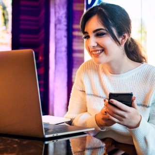Image of woman looking at laptop while holding mobile phone