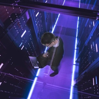 Image of a man in a servers room looking at his laptop