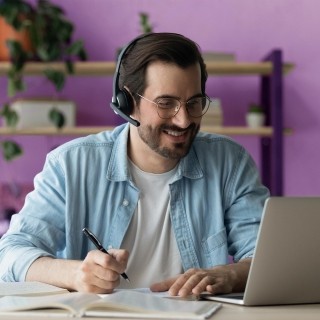 Person studying with headphones, notebook, and laptop at a desk