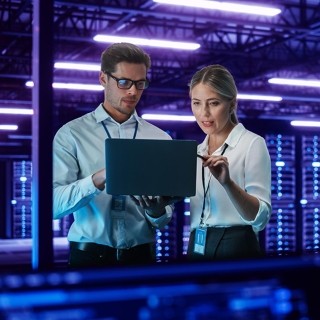 Image of man and woman discussing while holding laptop inside a server room