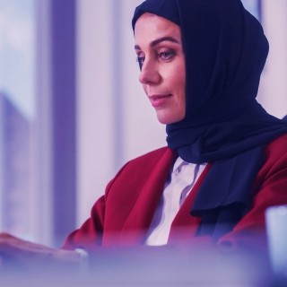 Professional in red jacket working on a laptop indoors with blurred background.