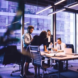 Business team meeting in a modern office with large windows overlooking a nearby building.