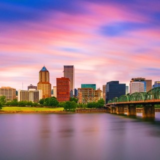Vibrant city skyline at sunset with riverfront and modern bridge.