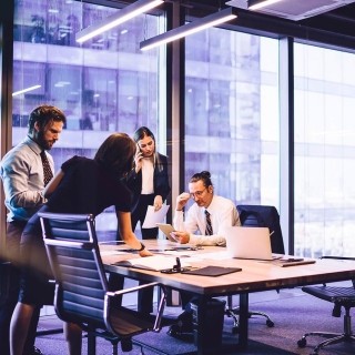 Business team meeting in a modern office with large windows overlooking a nearby building.