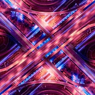 Aerial view of a multi-level highway interchange lit with vibrant purple and blue lights at night.