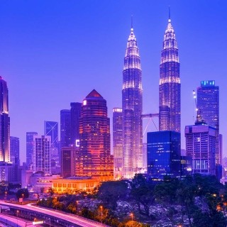 Iconic Kuala Lumpur skyline featuring the illuminated Petronas Twin Towers at dusk.