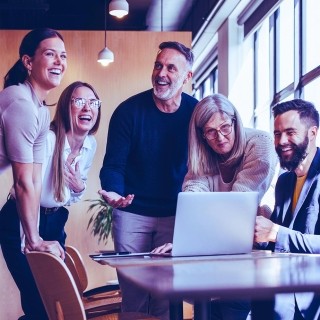 Team collaborating around a laptop in a modern office environment, discussing digital strategy and AI-driven solutions.