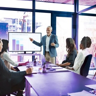 Business team meeting in a modern conference room with a presenter explaining data charts on a digital screen during a strategy discussion.