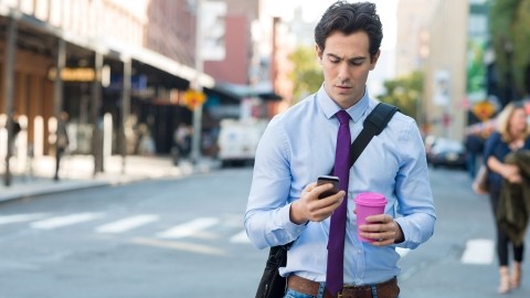 Image of man, cup in hand, texting on the street