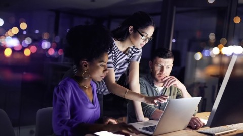 Image of team discussing in front of a laptop at night