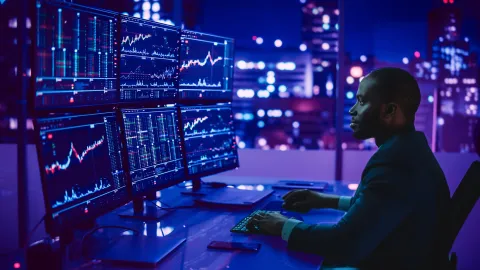 Image of professional trader in front of multiple screens with graphics