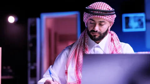 Image of person in front writing in front of laptop