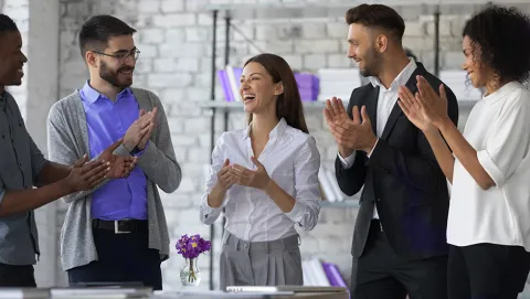 Diverse business team applauding in a modern office with brick walls and bookshelves.