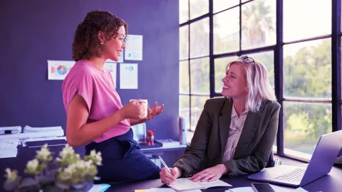 Office discussion between colleagues with notes and laptop in a modern workspace.