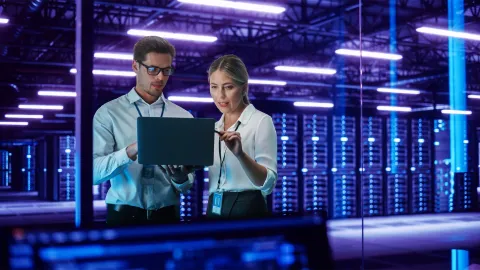 IT specialists analyzing data on a laptop in a secure, high-tech server room.
