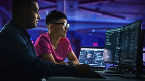 Cybersecurity experts analyzing code on multiple monitors in a high-tech environment.