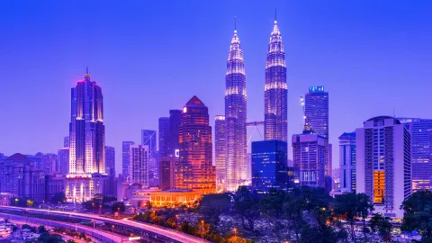 Iconic Kuala Lumpur skyline featuring the illuminated Petronas Twin Towers at dusk.