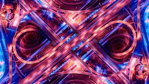 Aerial view of a multi-level highway interchange lit with vibrant purple and blue lights at night.