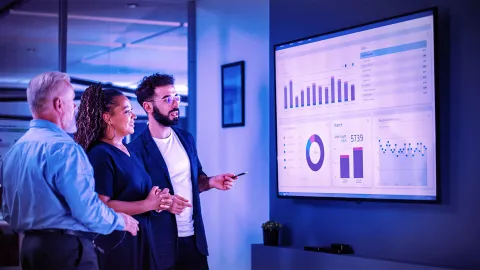 Team reviewing business analytics dashboards on a large digital display in a modern office